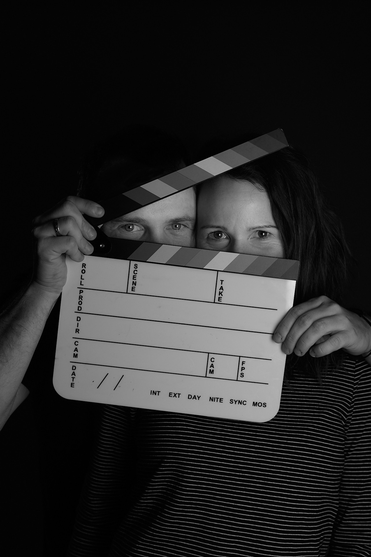 Das Team von Sonnen Media in Aktion - Schwarz-Weiß-Foto von Helena und Tobias, das hinter einer Filmklappe hervorschauen.